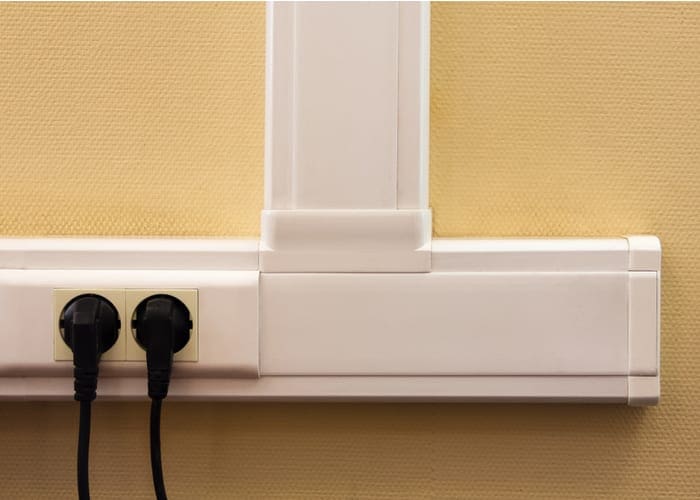 White cable channel with electrical outlets on a yellow wall, where two black plugs are inserted as an option for a piece on how to hide tv wires
