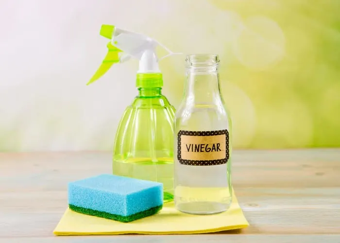 Chemical free home cleaner products concept. Using natural destilled white vinegar in spray bottle to remove stains. Tools on wooden table, green bokeh background, copy space as a way to make a natural weed killer