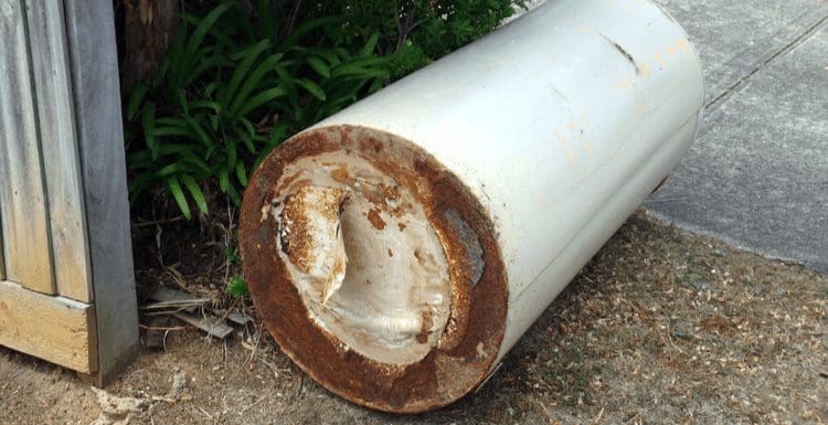 For a piece on how old is my water heater, such an appliance rusts on a driveway next to a fence