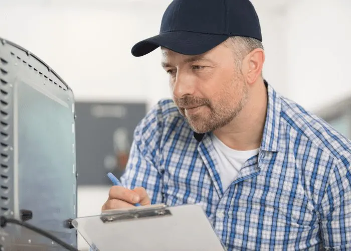 Image of an appliance repair man wearing a navy cap and holding a clipboard for a piece on how old is your water heater