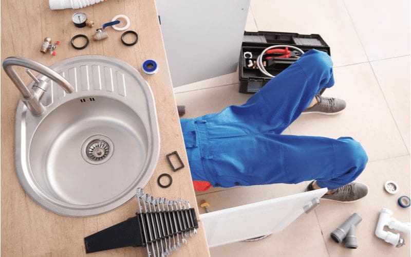 For a piece on how to install a sink drain, a man works under the sink with his feet sticking out from the cabinet