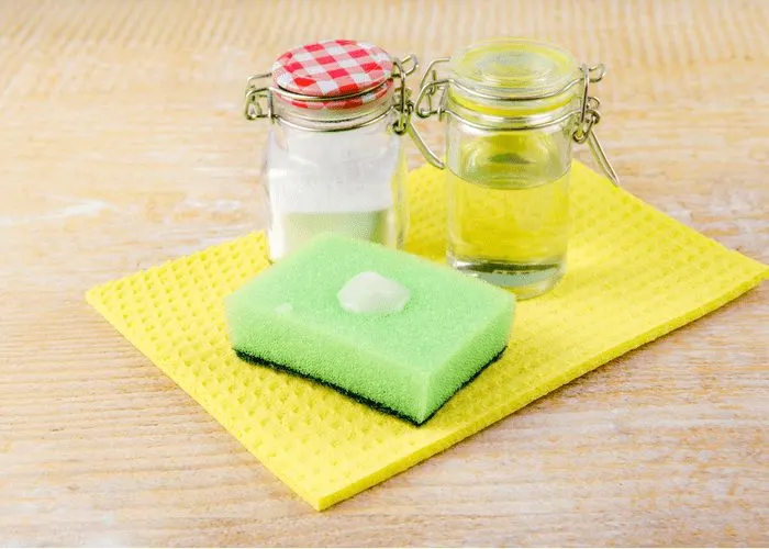 Homemade carpet stain cleaners sit on a counter alongside a sponge and vinegar