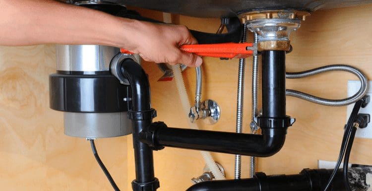 For a piece on how to install a sink drain, a plumber tightens a drain flange with a wrench