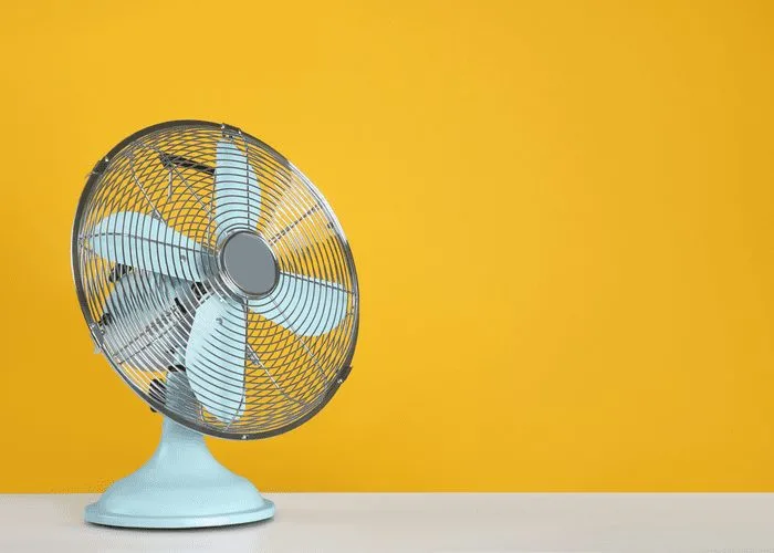 To help answer how long does liquid nails take to dry, a table fan sits on a simple wooden table in front of an orange wall