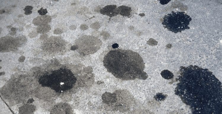 For a piece on how to remove oil stains from concrete, an image of a concrete slab with tons of oil stains of various sizes and shades