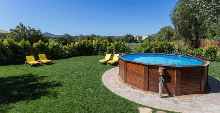 For a piece on how to level ground for pool, an above-ground pool sits on a concrete base next to a yard with yellow chairs