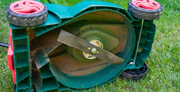 For a piece on how to remove a lawn mower blade, a mower sits on its side on green grass with a dirty blade below