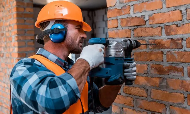Construction worker drilling brick with and wearing ear protection