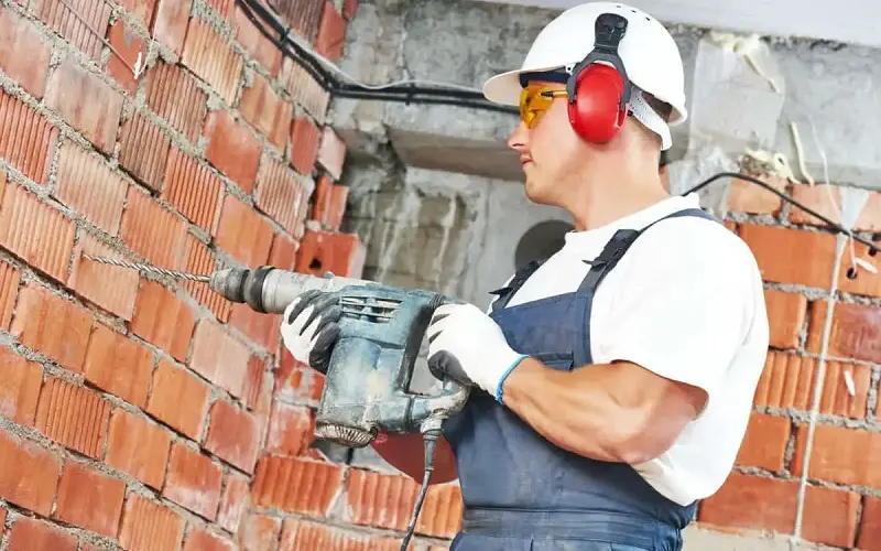 Construction worker wearing safety gear when drilling bricks