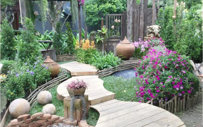 Landscaping idea of a wooden bridge above a fountain with lots of flowers and statues