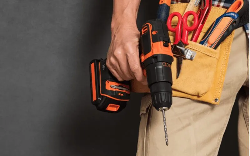 Close up of a handyman with a tool belt holding a drill for a piece on how to drill into brick