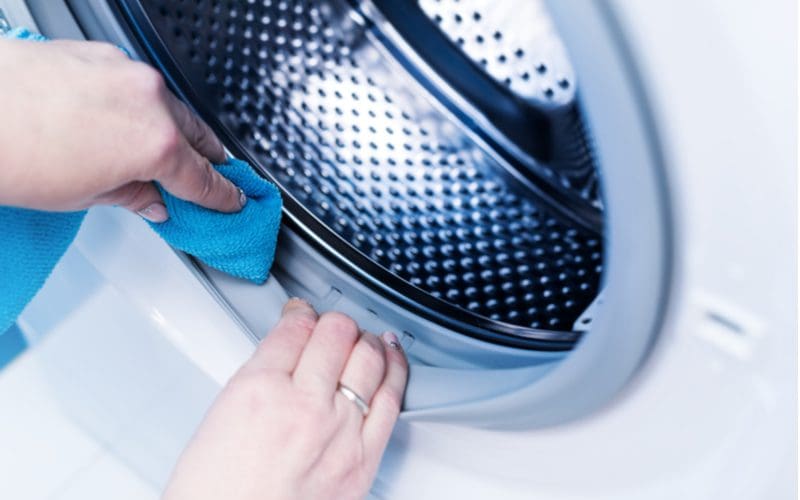 Hand cleaning a washing machine drum with a microfiber towel because it smells