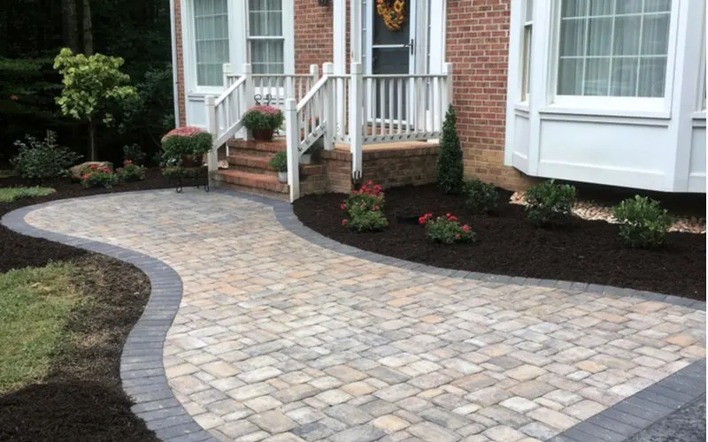 Paver patio idea with a simple bean design next to dark mulch beds in the front of a house