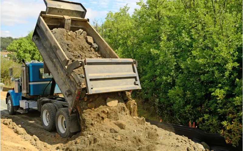 Dump truck pouring out a bunch of dirt for a piece on top soil cost