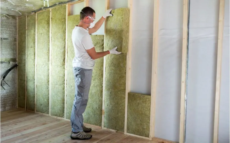 Man installing unfaced insulation on a wall with standard spaced studs