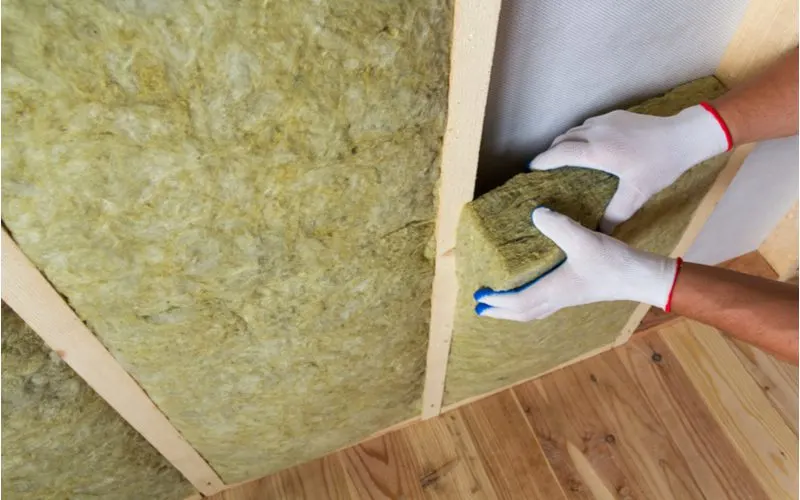 Unfaced insulation being shoved into the studs of a home's walls by a guy in white and blue gloves