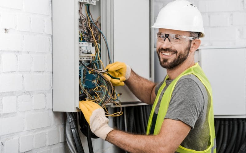 Handsome electrician working on a breaker box and smiling while wearing a hard hat
