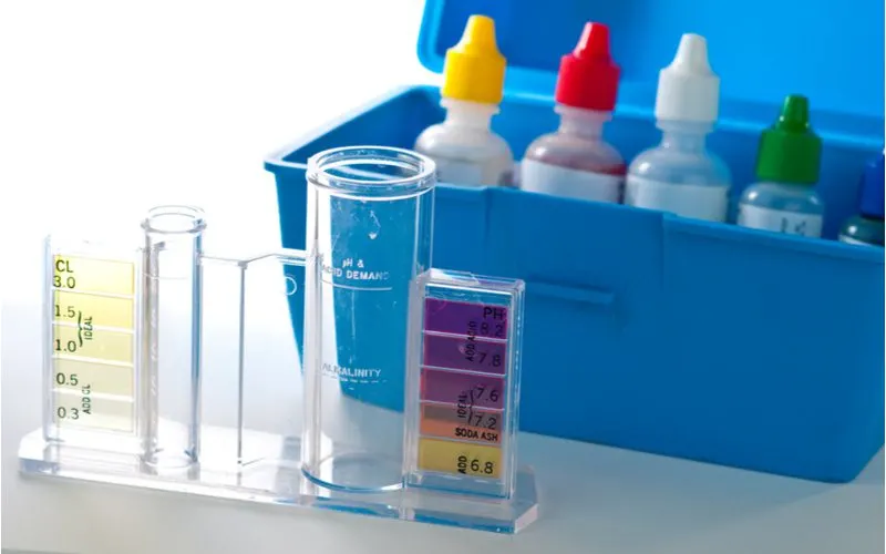 Swimming pool water test kit with chemicals and a beaker on a table next to a blue container
