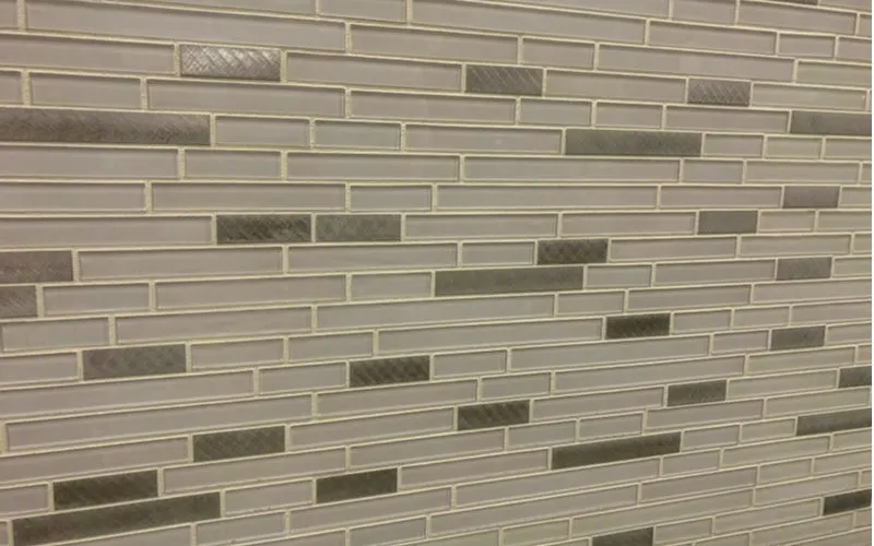 Sanded grout on a multi-color glass backsplash to illustrate the difference between sanded vs unsanded grout