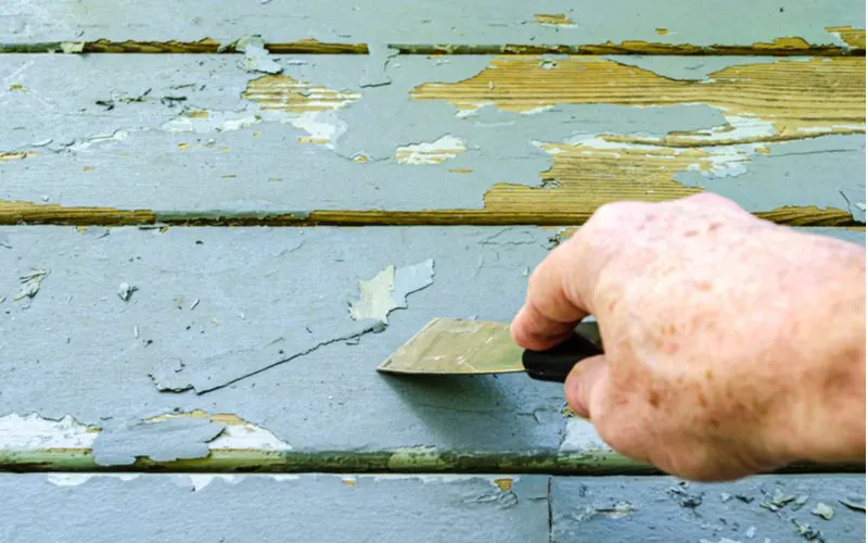 man's hand scraping old gray paint off wooden boards for a piece on how to remove stain