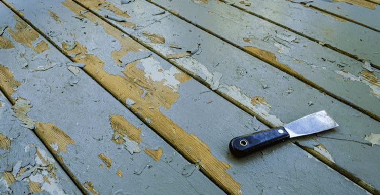 For a piece on how to remove paint from wood, a deck with flaking paint sits next to a putty knife