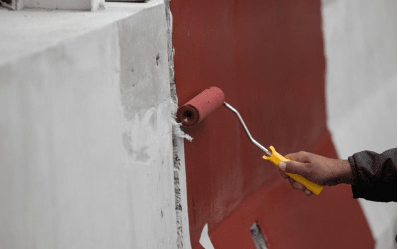 Man painting cinder block wall red with a roller