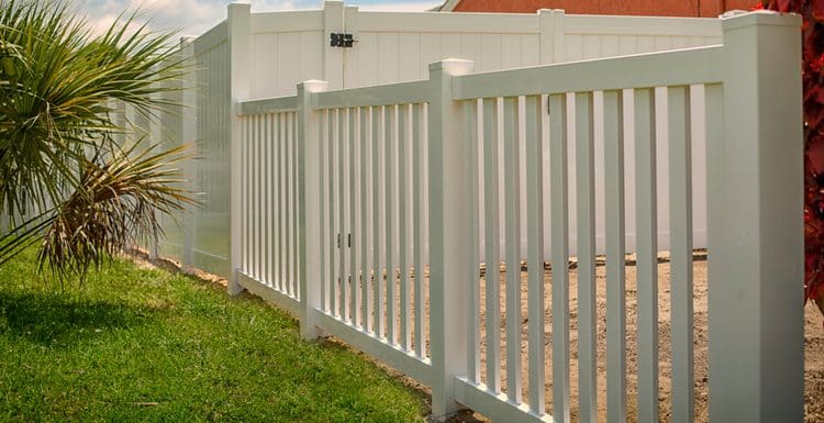 Featured image for a post on vinyl fencing cost featuring a solid and picket fence in white next to a palm tree and brown stucco home