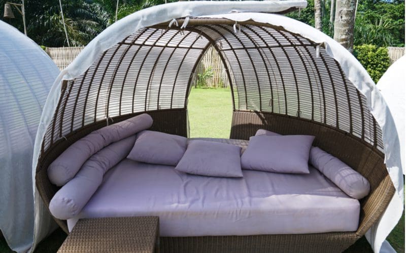 Brown wood and white fabric daybed with a canopy above a grey cushioned and pillowed bed