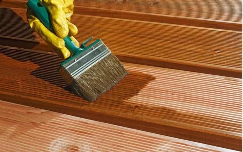 Person staining pressure treated wood with yellow gloves and a metal and composite brush