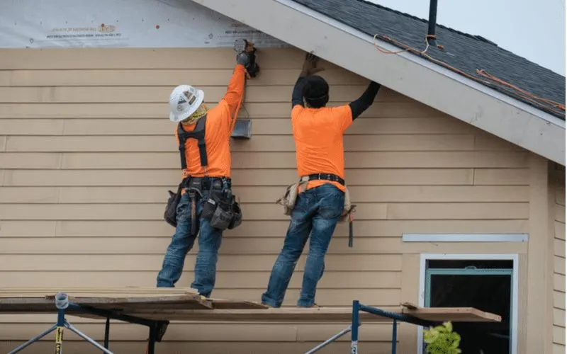 Construction workers standing on scaffolding and installing a horizontal type of vinyl siding