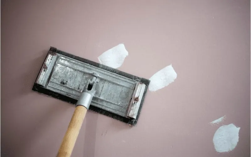 For a piece on how to remove drywall anchors, a guy pole sands a spackled wall