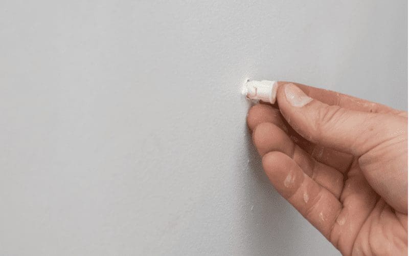 Man pushing a drywall anchor plug into the wall with his hand