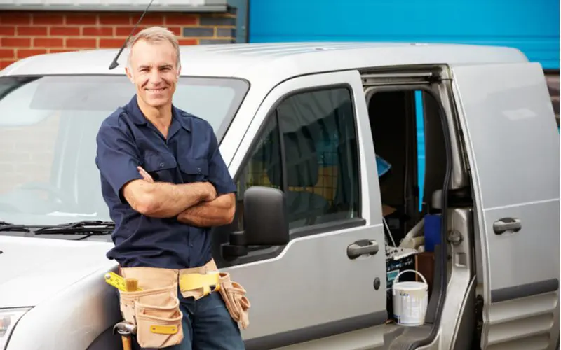 Man standing in front of a plumbing truck with a tool belt crossing his arms