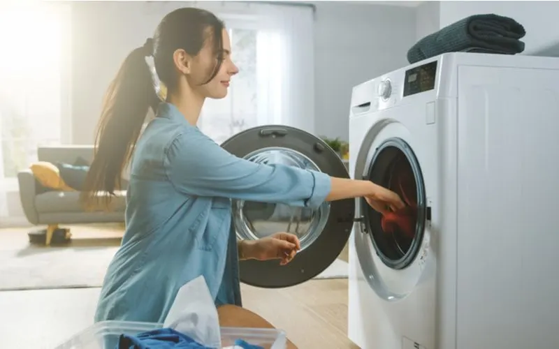 Woman loading laundry into a washer that uses he detergent and leaving the door open so it doesn't smell