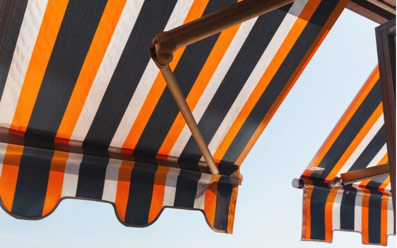 Image of a striped awning extended manually against blue sky