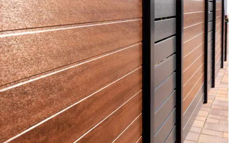 Wood colored vinyl fence cost illustrated by a black and wood grain style fence with horizontal slats