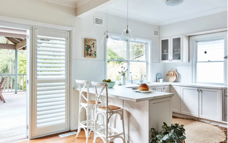 Interior photography of a fresh white Hamptons style kitchen with breakfast bar, cross back bar stools, polished floor boards and a door way opening up to a back deck