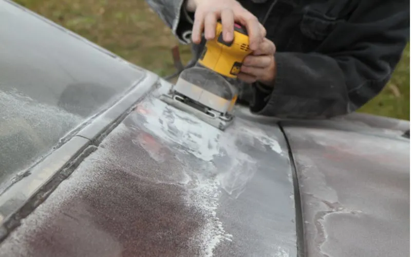 Guy sanding the paint off a chrome vehicle hood