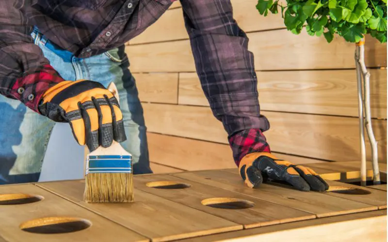 To help answer can you paint over stain, a guy in gloves and a plaid flannel shirt stands outside and stains wood furniture
