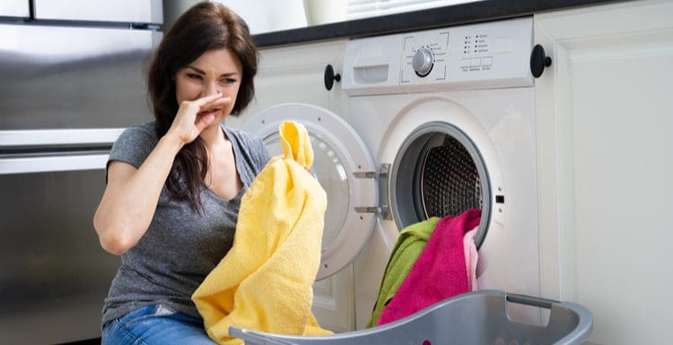 Woman covering her nose because her washing machine smells and holding clothes up