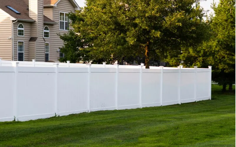 To illustrate factors affecting the vinyl fence price, a white vinyl fence in a suburban backyard next to green grass sits on a summer day