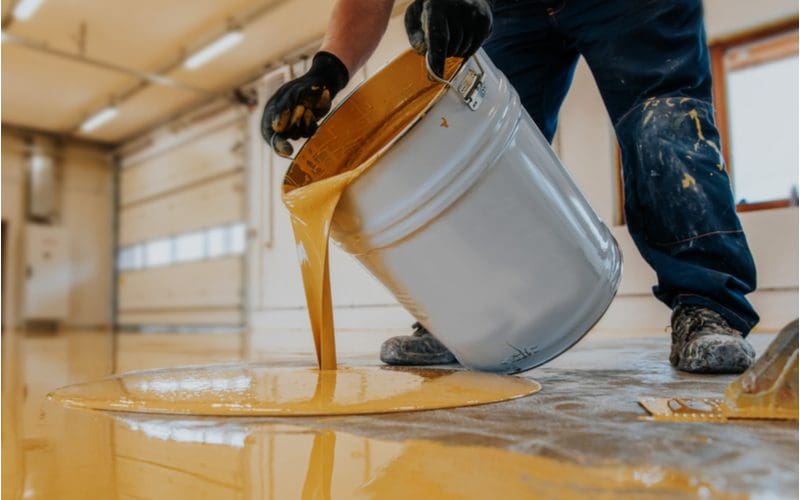 Man applying concrete paint with yellow resin epoxy mixed in to a garage or factory floor