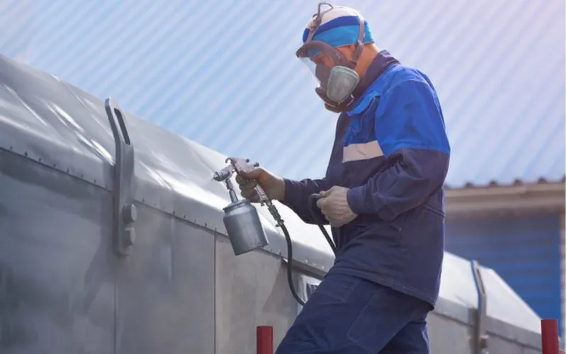 Guy spraying metal primer onto a metal building wearing a mask and overalls