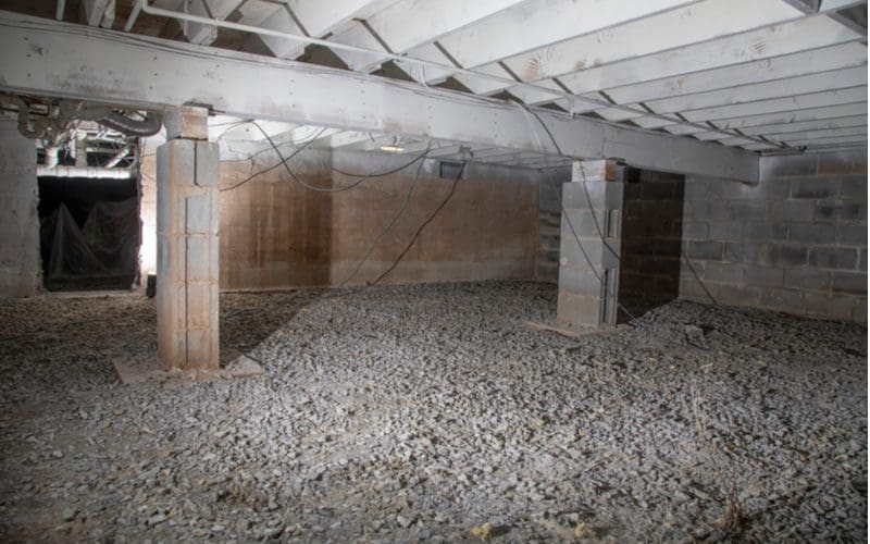 Image of an uninsulated crawl space with corrugated metal pieces running width-wide above a rock floor