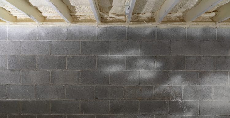 Crawl space insulation below a basement with rocks and spray foam next to a grey block wall