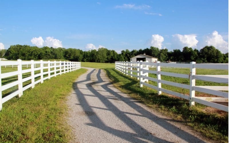 Split rail vinyl fence on either side of a dirt road leading up to a farm