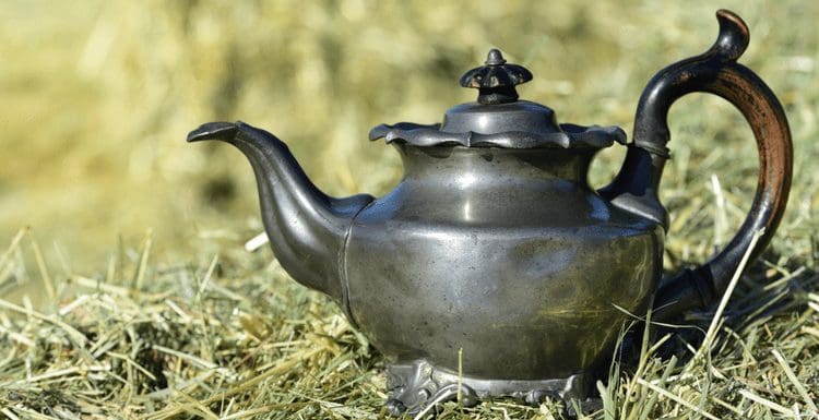 As a featured image for a piece on how to clean pewter, an antique coffee pot sits on grass