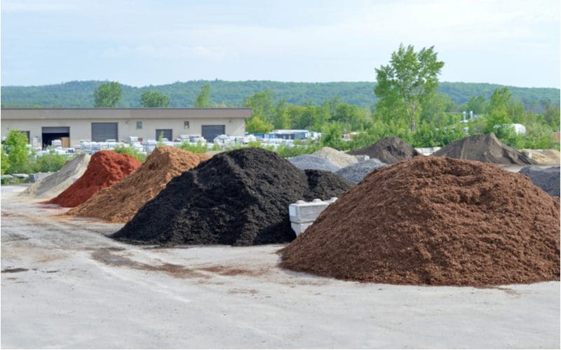 various stone and cedar mulch piles separated into various types for packaging in the warehouse seen in back