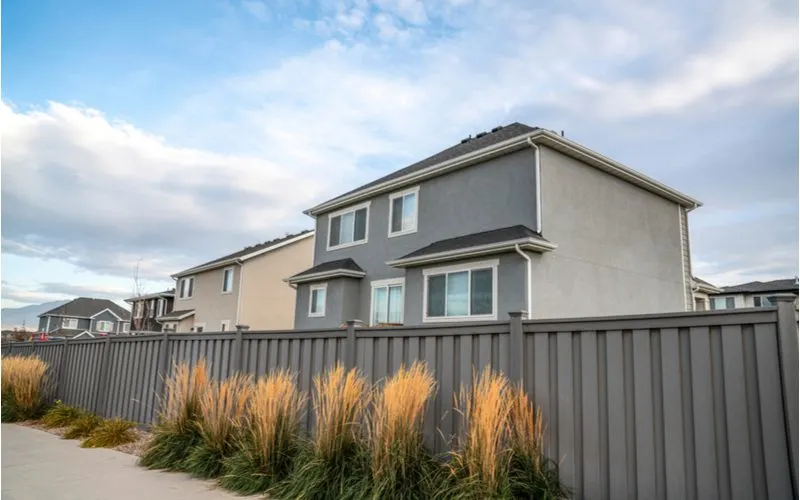 Grey vinyl shadowbox fence sits next to a simple gray home with ornamental grass outside