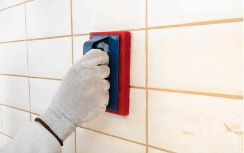To illustrate sanded vs unsanded grout differences, a sponge moves across white tile backsplash